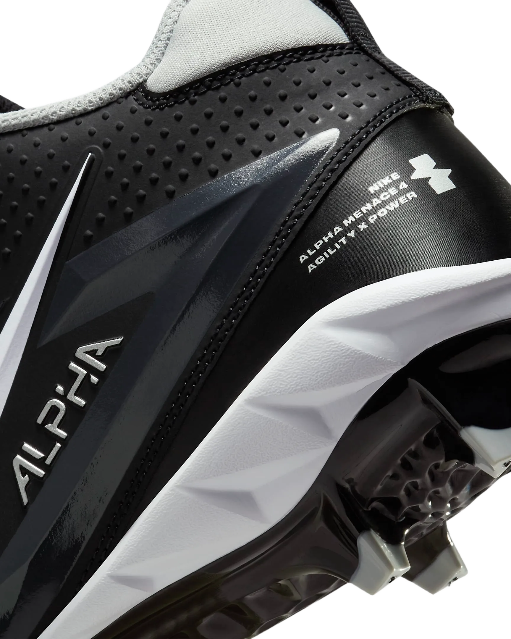 Close-up of Nike Alpha Menace Varsity 4 black and white cleat with agility and power features visible on sole and side.